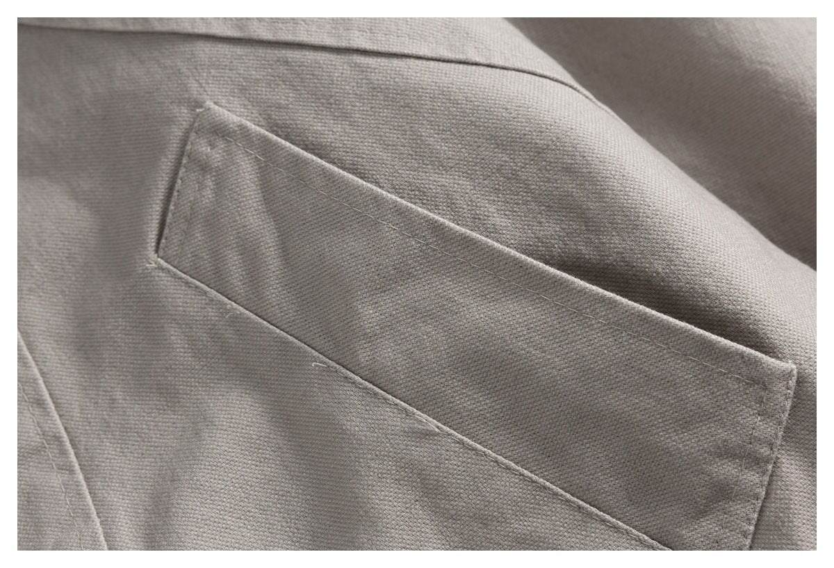 Close-up of a rectangular stitched pocket on the textured light gray jacket fabric.