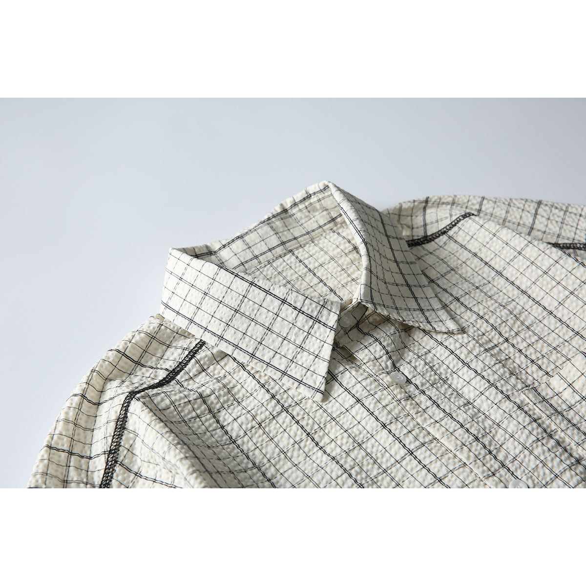 Close-up of a cream button-up shirt with a black windowpane check, showing the pointed collar and shoulder seam.