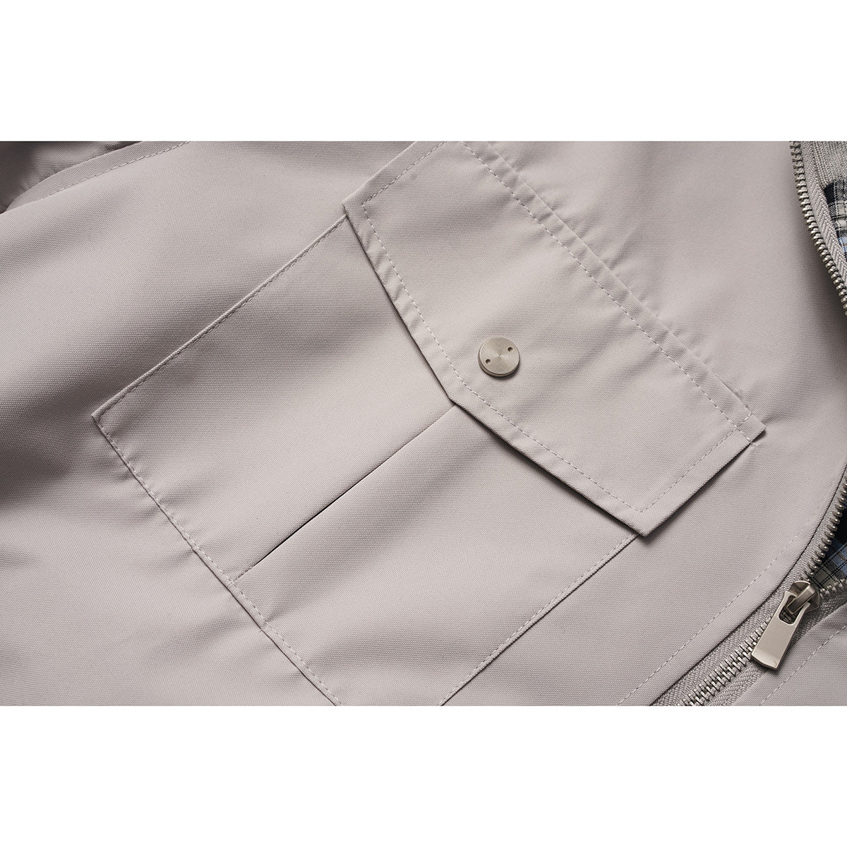 Close-up of a light gray jacket's flap pocket, button, stitching, and front zipper.
