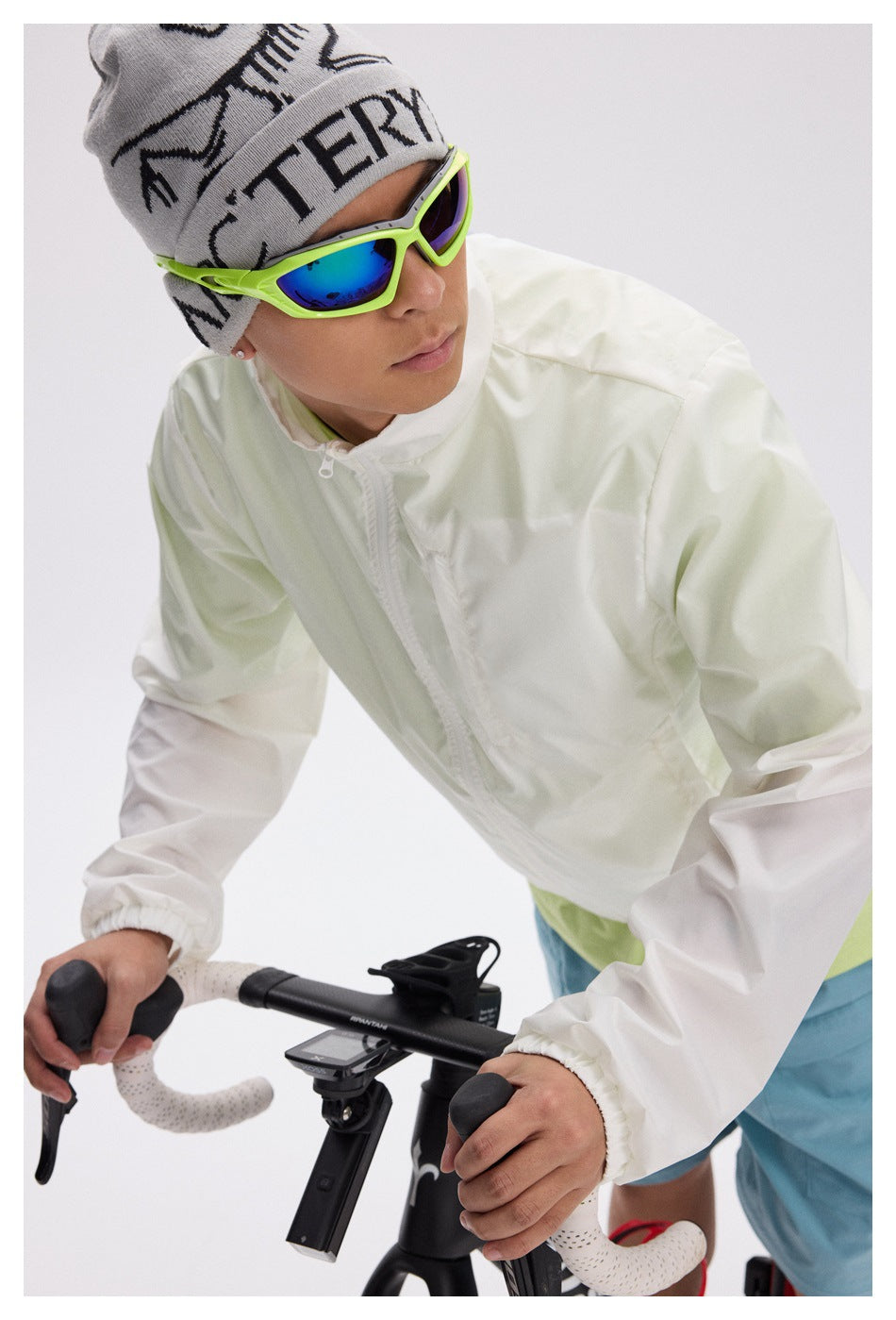 Cyclist wearing a white zip-up windbreaker, shown from the front while leaning over a bicycle.