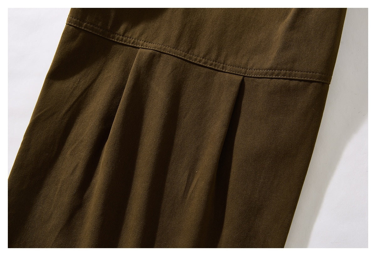 Close-up of olive-brown trouser fabric with a horizontal stitched seam and pleat.