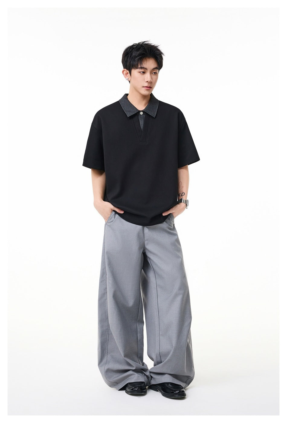 Full-length view of a model wearing a black polo-style shirt with a charcoal collar and loose light gray trousers.