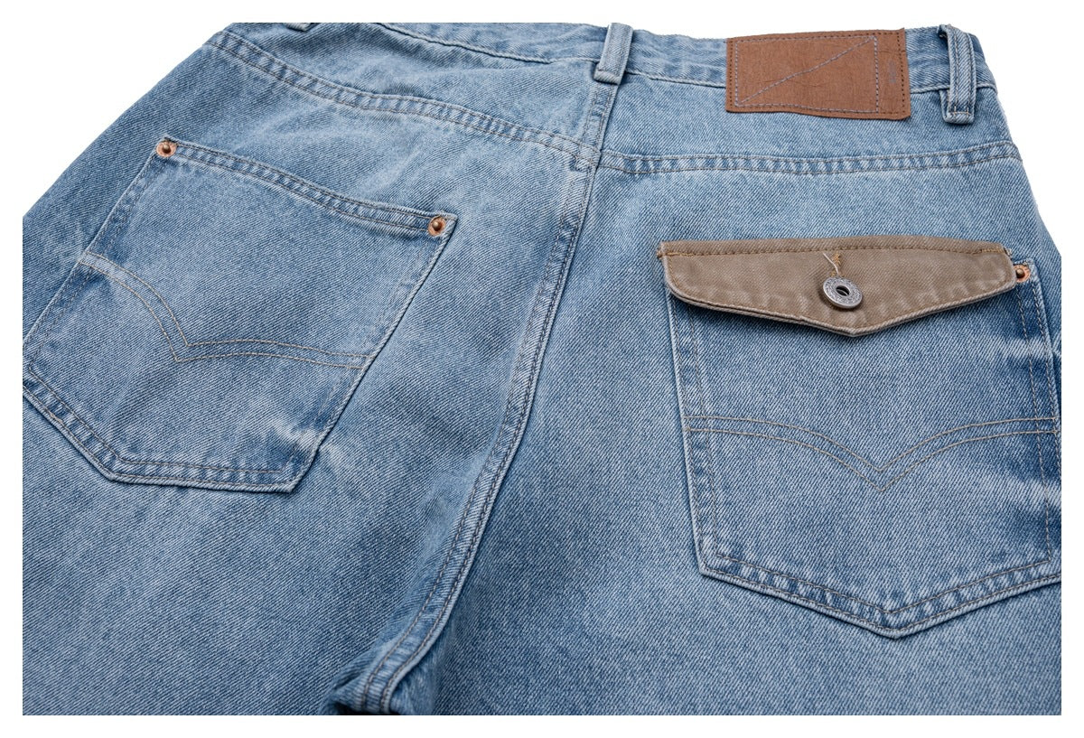 Close view of the back of light blue jeans, showing two pockets, a brown waistband patch and a flap pocket.