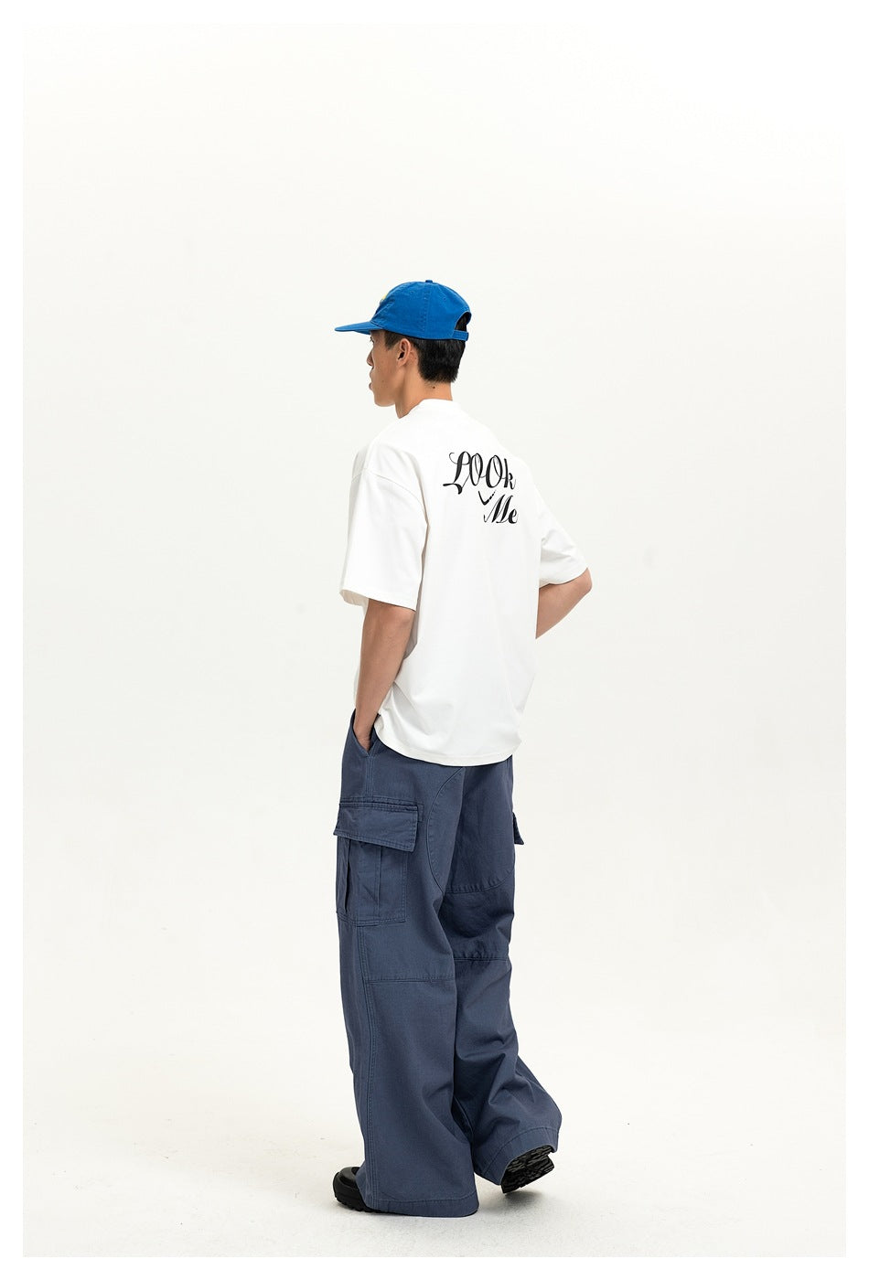 Rear view of a model in blue wide-leg cargo pants and a white graphic T-shirt, wearing a blue cap.