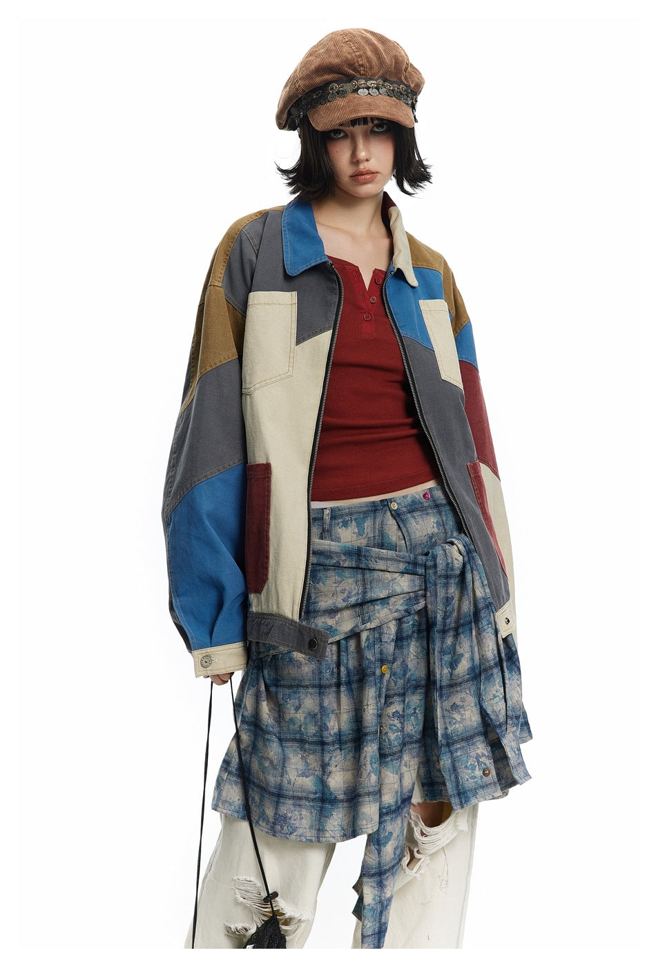 Model wearing a multicolor patchwork jacket with cream pockets, a red top, and a blue plaid skirt.