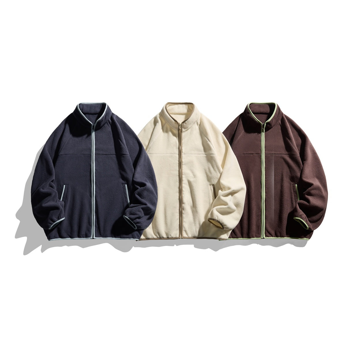 Three front-facing stand-collar zip fleece jackets in navy, cream, and dark brown with contrasting trim.