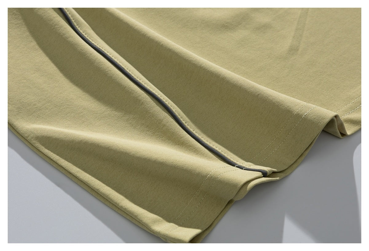Close-up of the pale olive T-shirt's lower hem and dark piping detail.