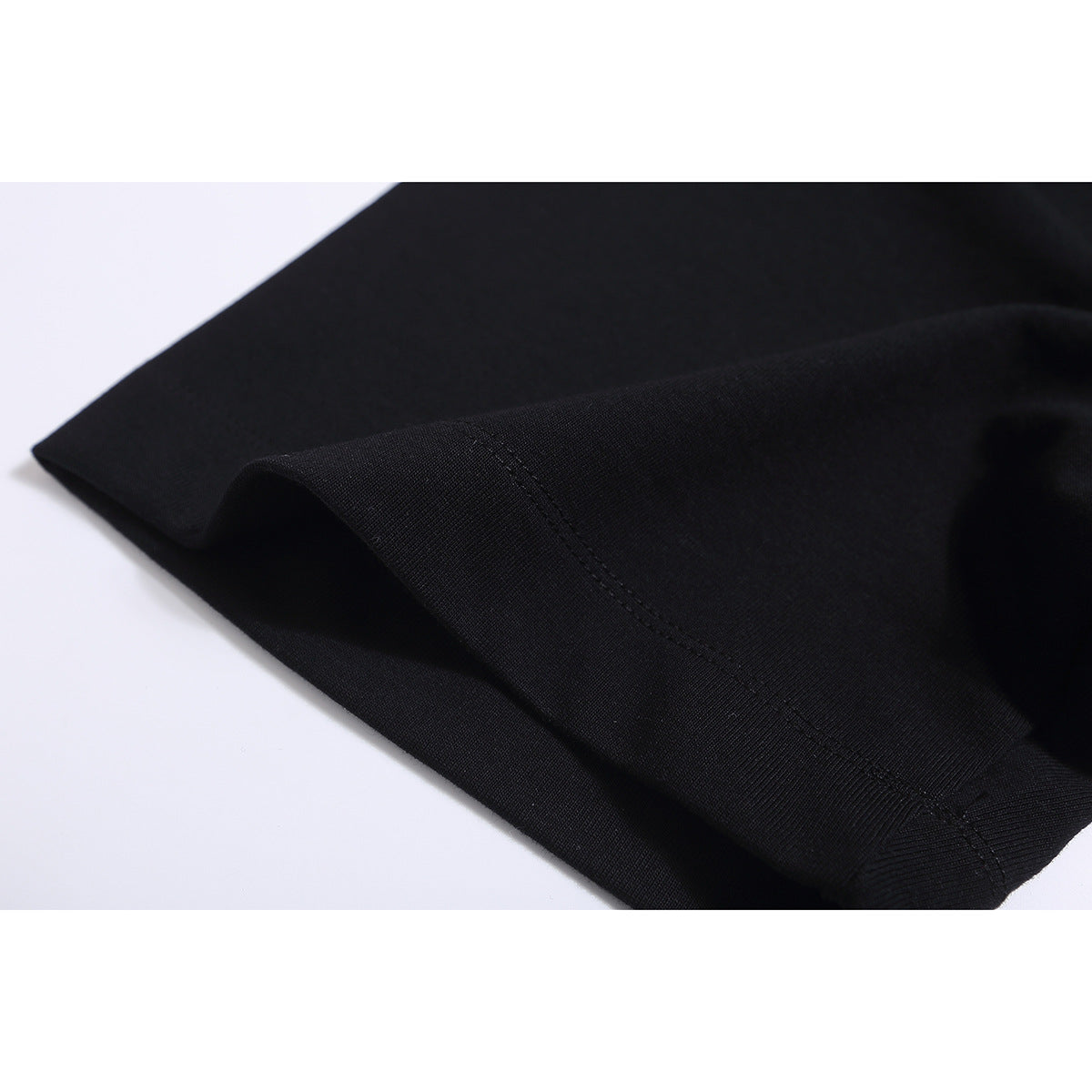 Close-up of black T-shirt fabric folded to show a stitched seam.