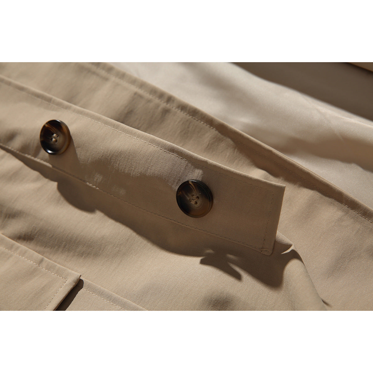 Close-up of a tan coat sleeve tab with two dark buttons and visible stitching.
