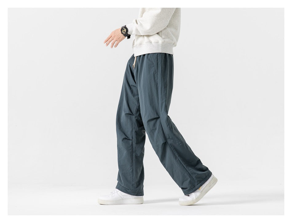 Cropped model wearing loose slate blue-gray pants, shown from the side with white sneakers.