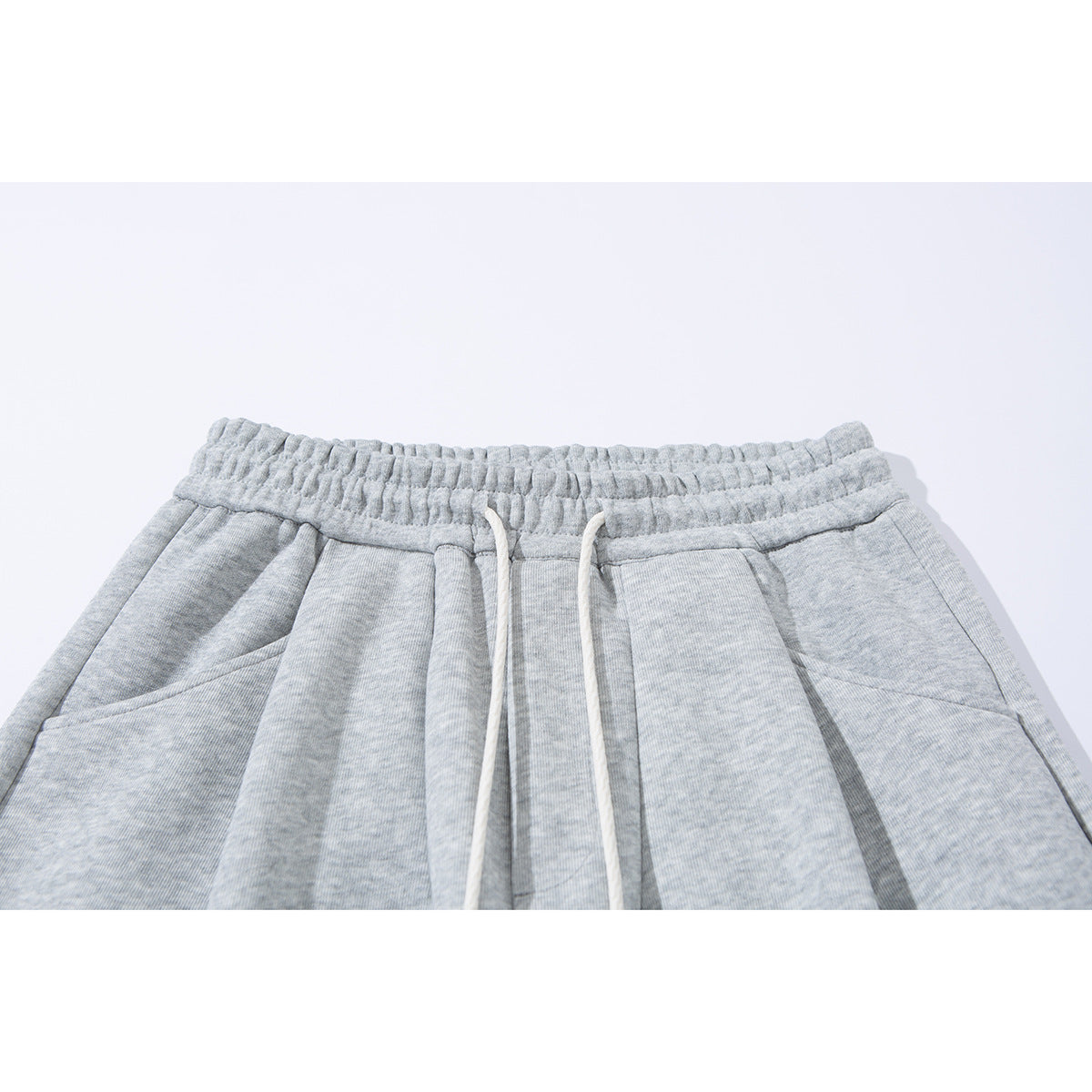 Close-up of light gray sweatpants with an elastic waistband, white drawstrings, and angled front pockets.