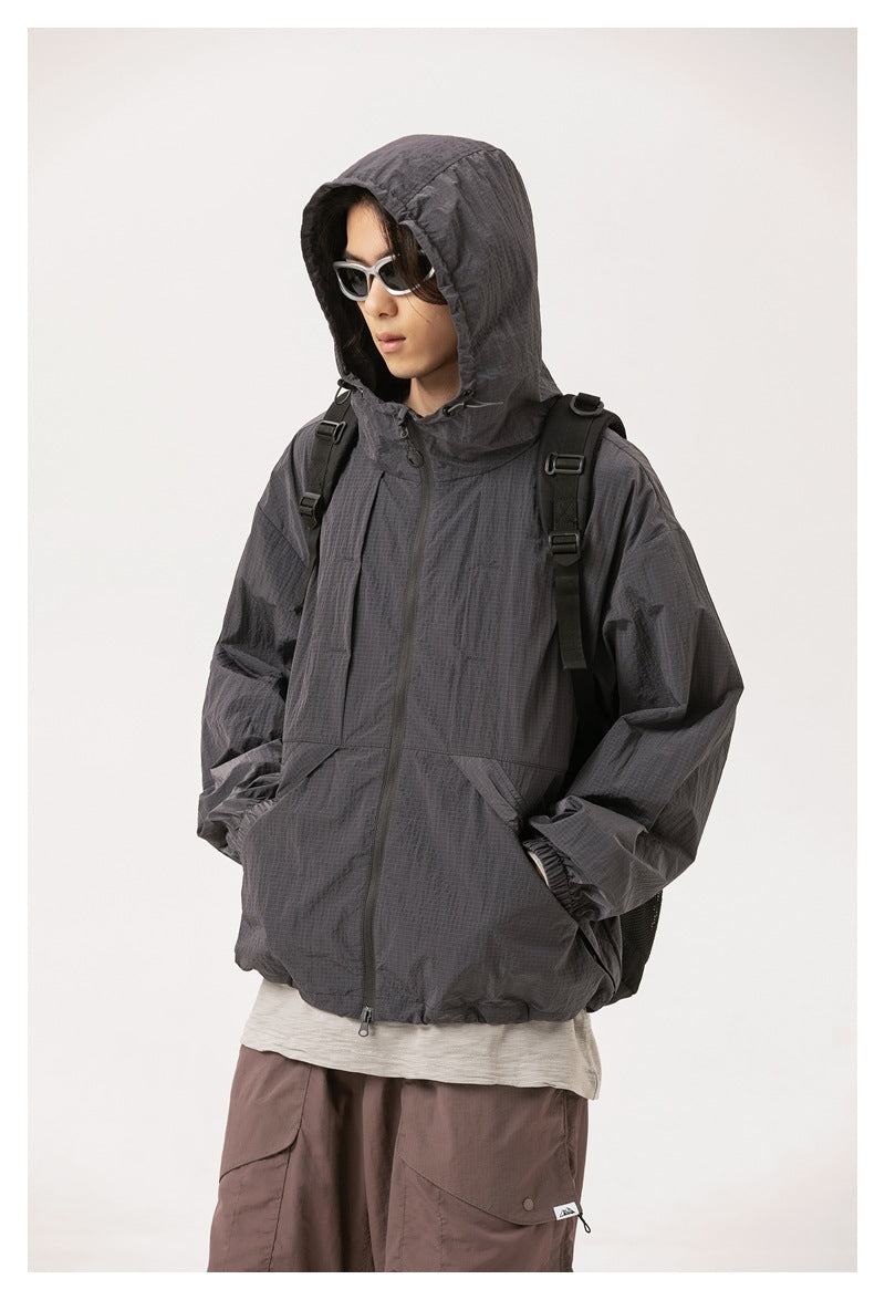 Model wearing a charcoal-gray hooded zip jacket with elastic cuffs and front pockets, shown with a backpack.