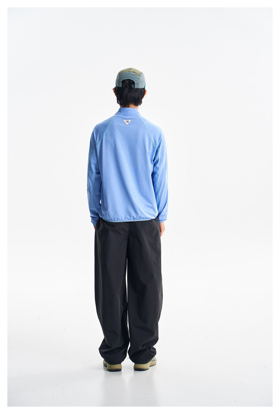 Back view of a model wearing a light blue pullover and loose black pants.