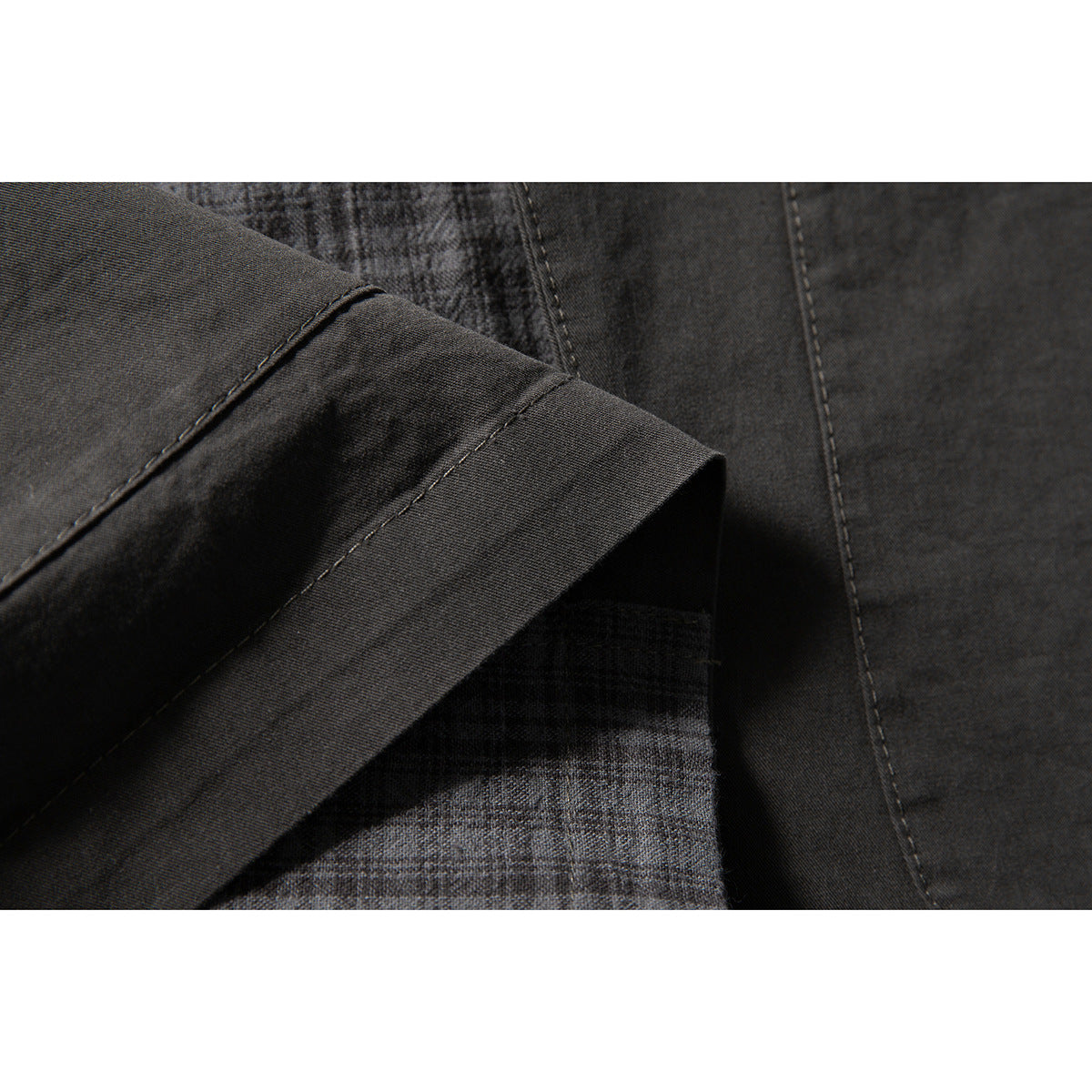 Close-up of a charcoal garment sleeve cuff and seams, with checked fabric visible underneath.