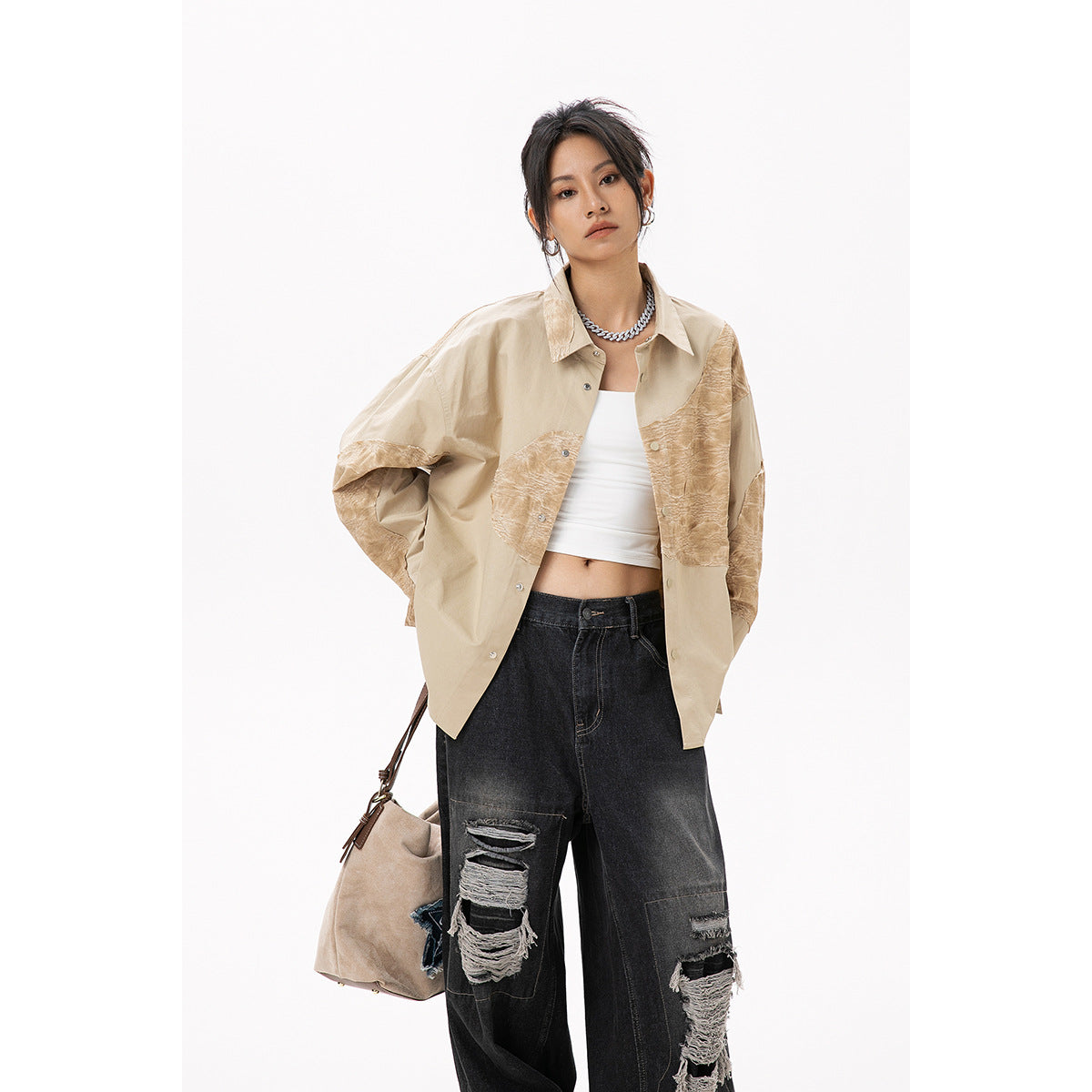 Model in a beige oversized shirt with tan textured panels and ripped black jeans, carrying a beige shoulder bag.