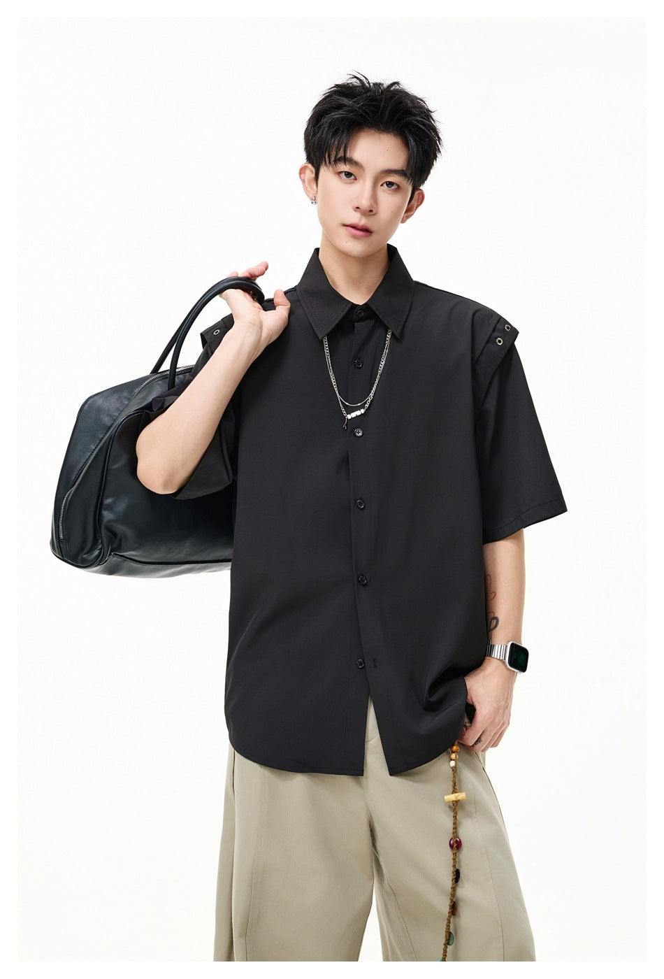 Model wearing a black short-sleeve button-up shirt with metal-eyelet shoulder tabs and beige wide-leg trousers.