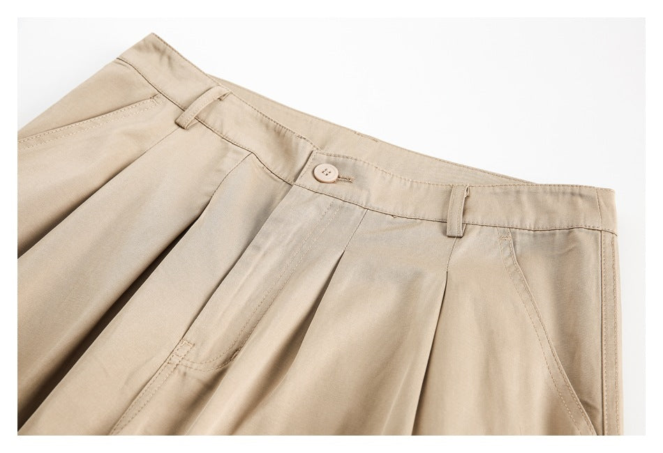 Close-up of beige trousers showing the buttoned waistband, belt loops, pleats, and slanted pocket.