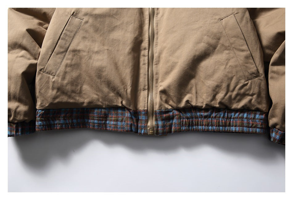 Close-up of a tan jacket’s front zipper, slanted pockets, and blue-brown plaid hem trim.