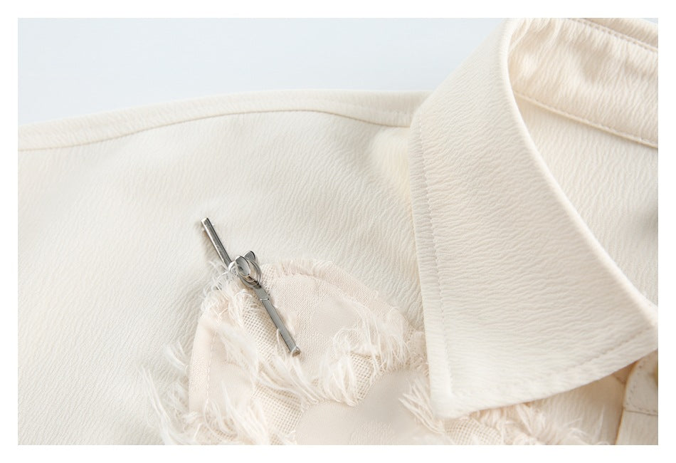 Close-up of a white shirt shoulder, collar edge, and small silver pin among frayed floral appliqué.