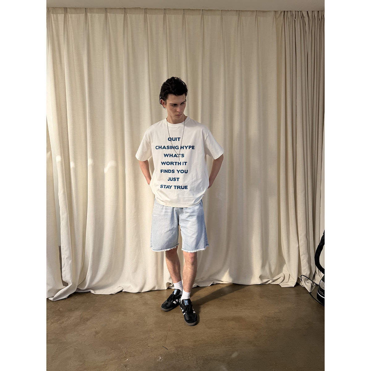 Model wearing a white T-shirt with blue text on the front and light blue cutoff denim shorts.