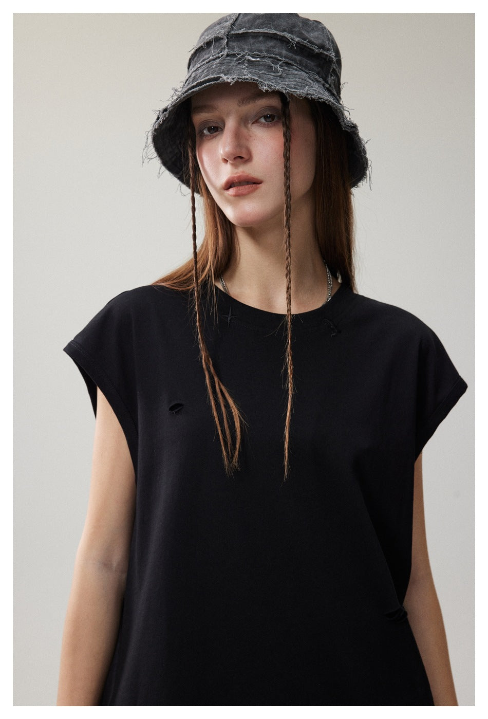 Model wearing a black sleeveless top with small distressed slits and a frayed dark bucket hat.