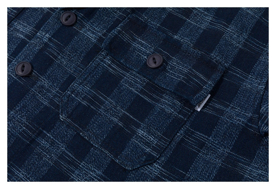 Close-up of a navy plaid shirt chest pocket with dark buttons and a small sewn label.