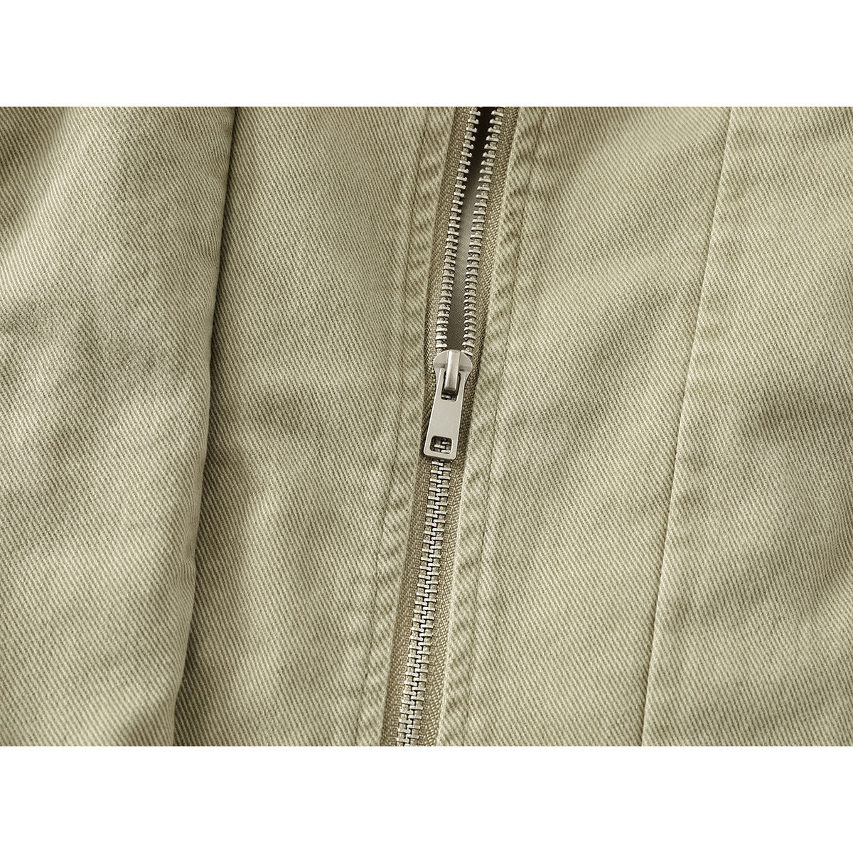 Close-up of a khaki jacket's central metal zipper and diagonal twill fabric.