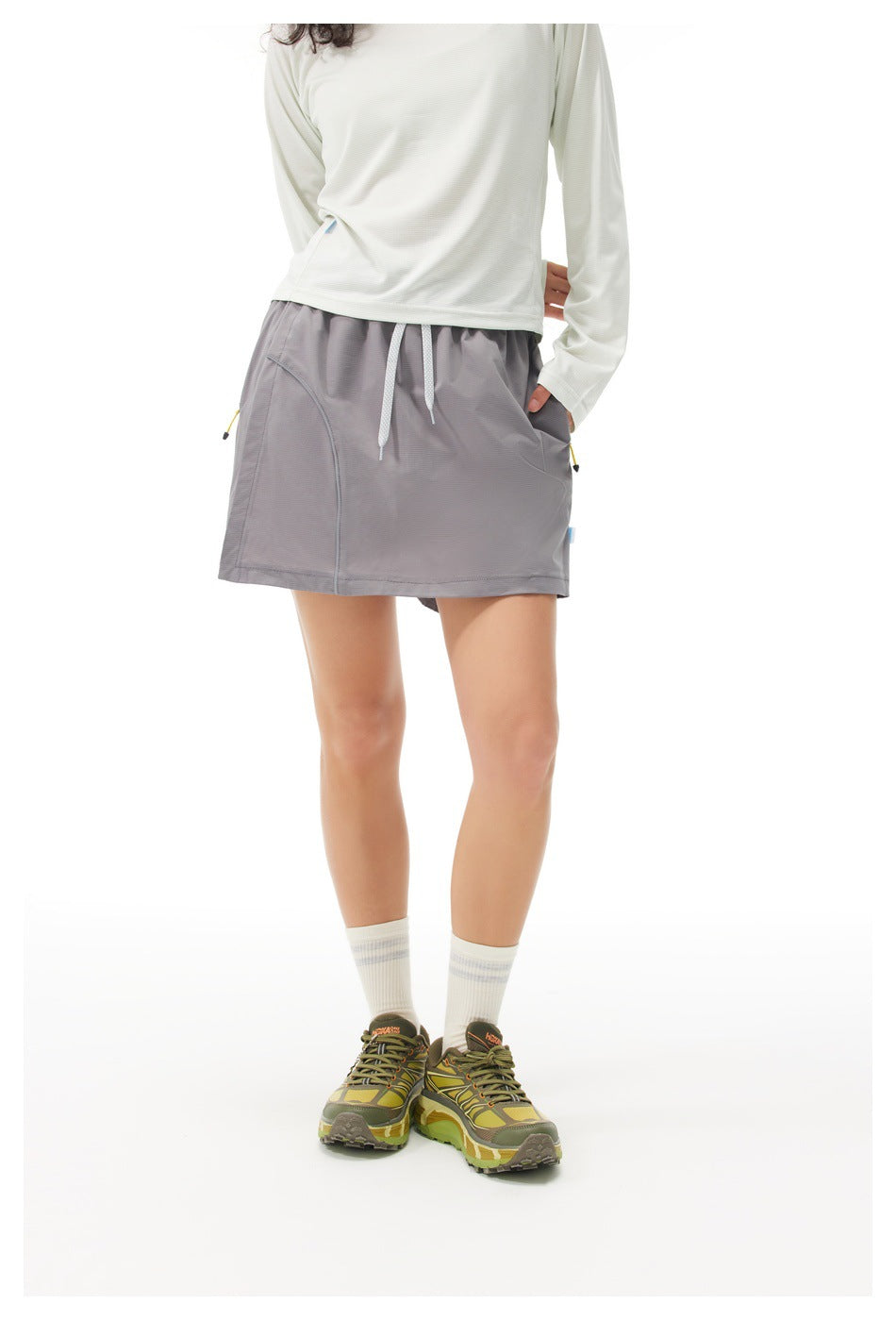 Model wearing a gray drawstring athletic skirt with curved front pocket seams and side pockets.