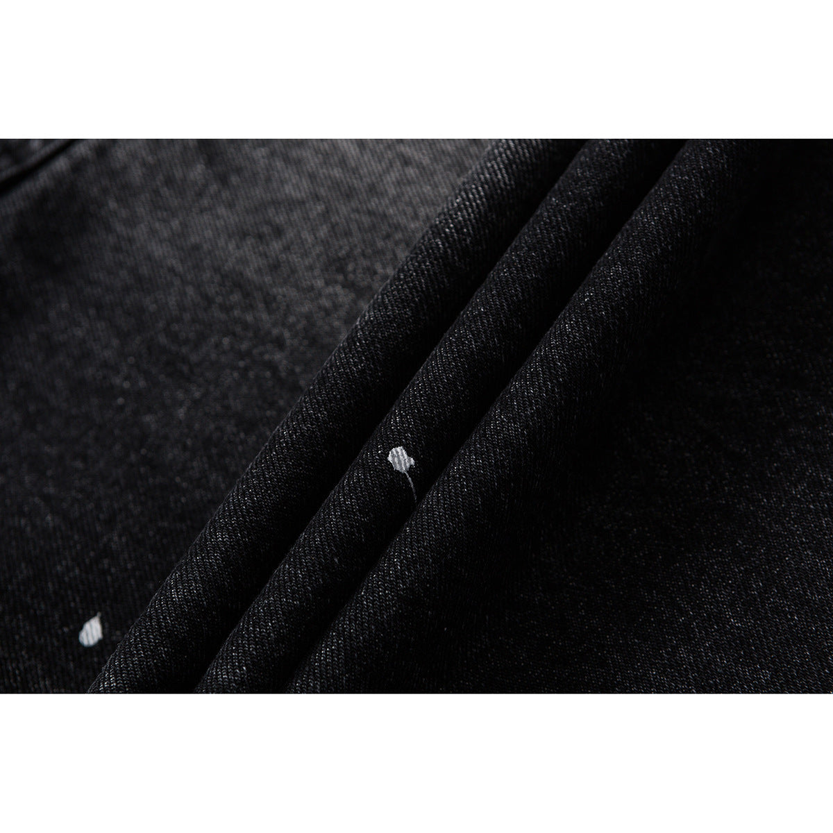 Close-up of dark denim folds with a visible diagonal weave and small white paint marks.