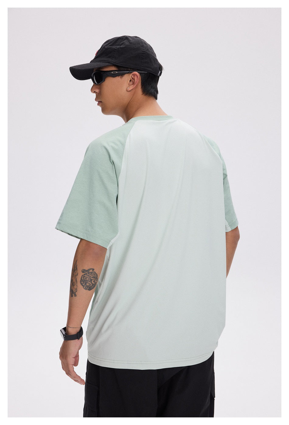 Model wearing the back of a pale sage T-shirt with a large white textured back panel and short sage sleeves.