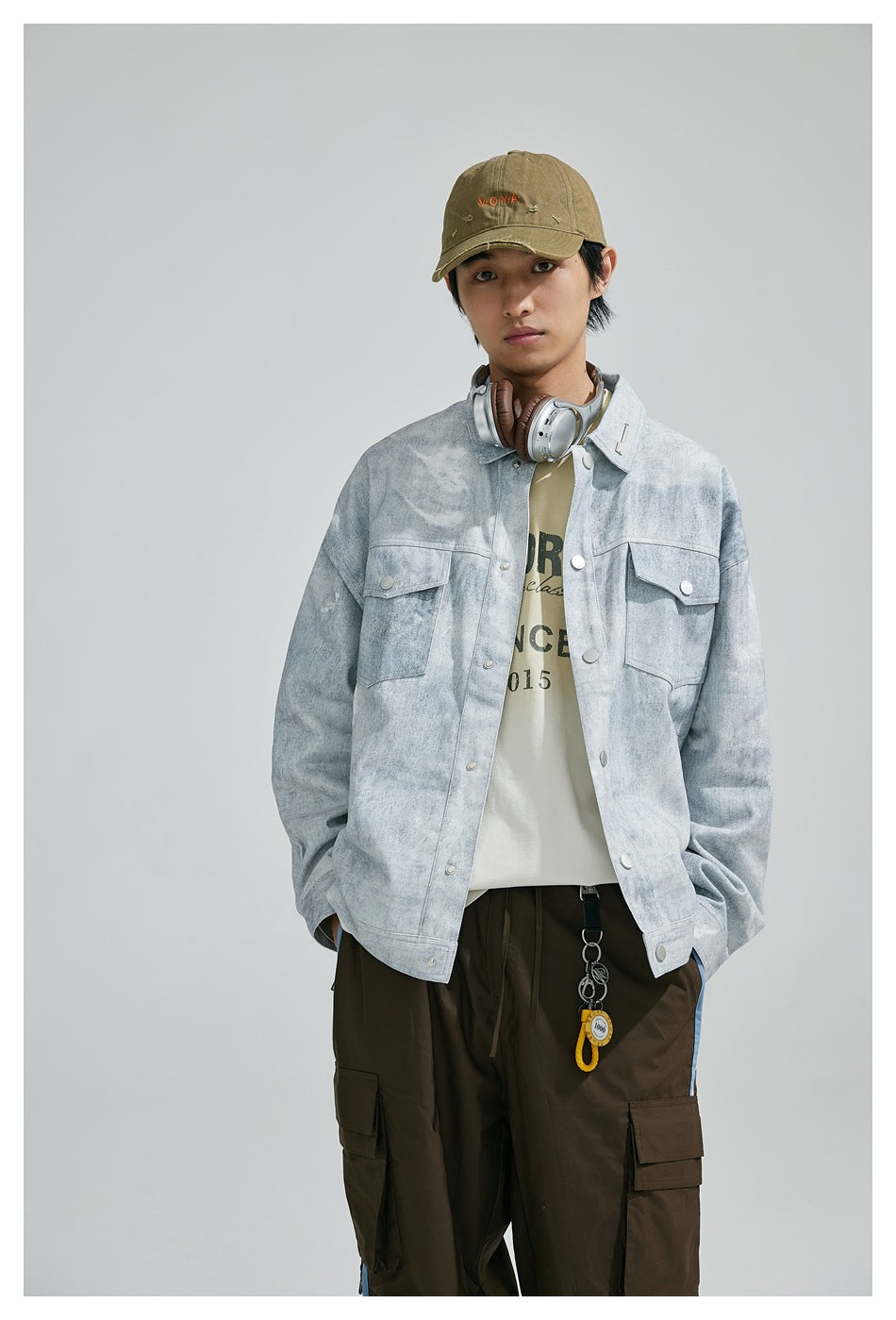 Model standing in light gray washed snap-front jacket with chest flap pockets, cream tee and brown cargo pants
