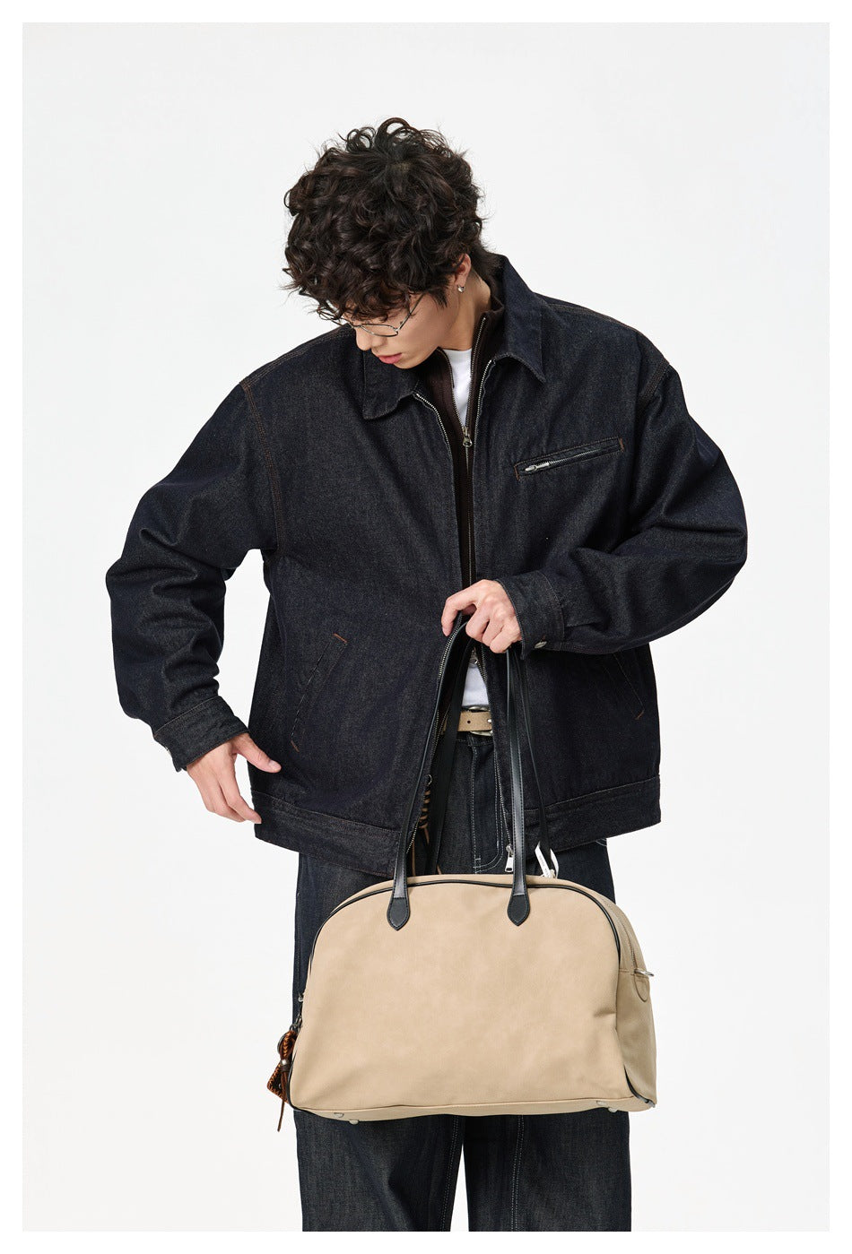Model wearing a dark indigo denim jacket with a pointed collar and zip chest pocket, holding a tan handbag.