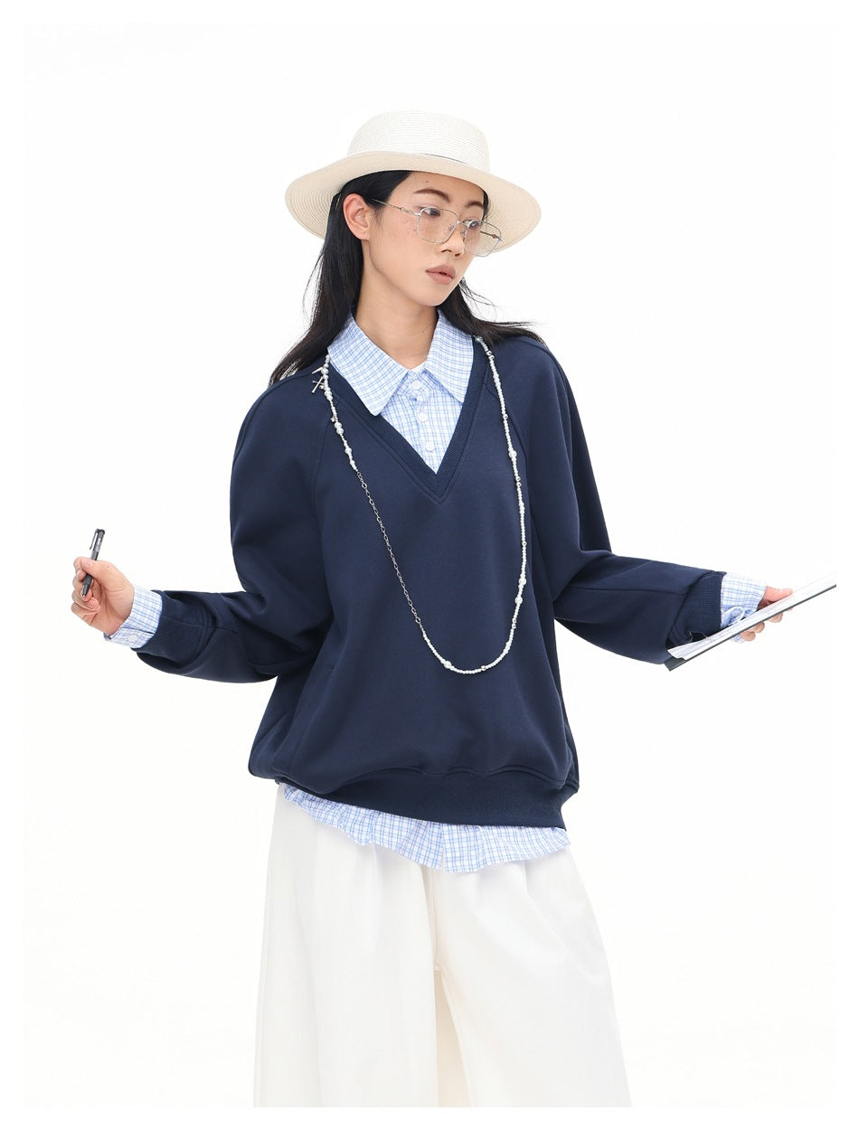 Model wearing a navy V-neck sweatshirt over a blue checked shirt, with the collar and cuffs visible.