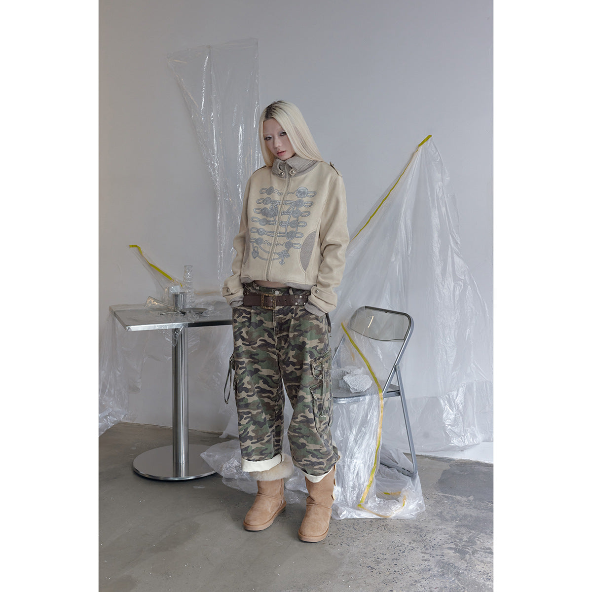Model wearing a beige graphic zip jacket with green camouflage cargo pants and tan boots.