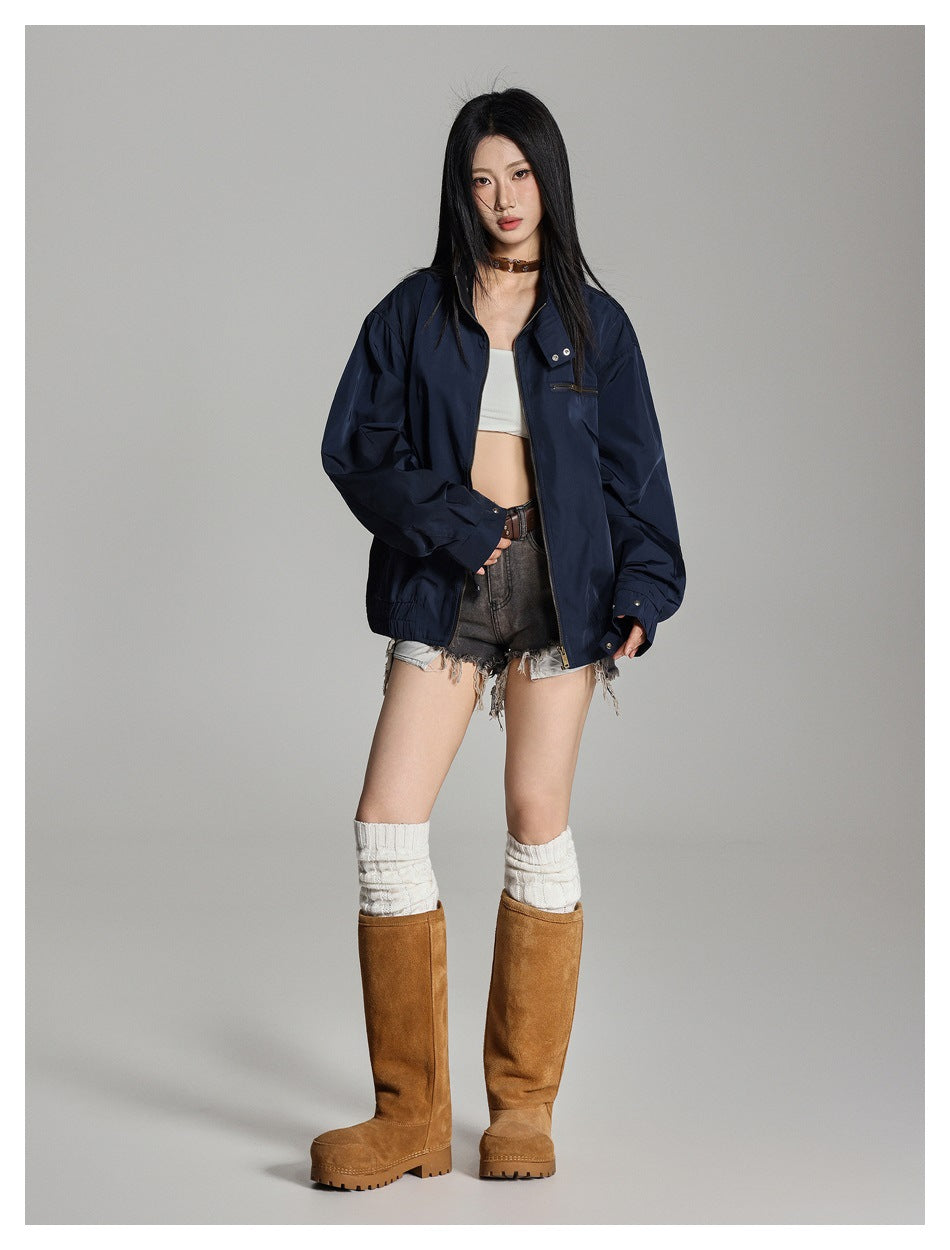 Model wearing an open navy zip jacket with denim shorts and tall tan suede boots, full-length view