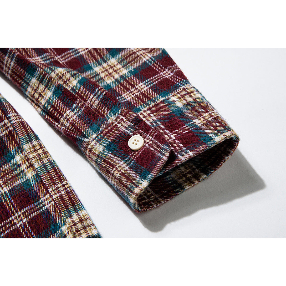 Close-up of the buttoned cuff on a burgundy, teal, and cream plaid shirt.