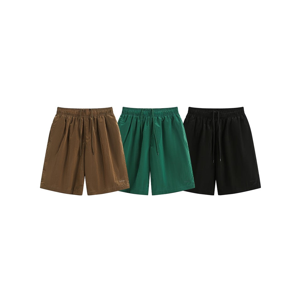 Three pairs of drawstring shorts displayed together in brown, emerald green and black.