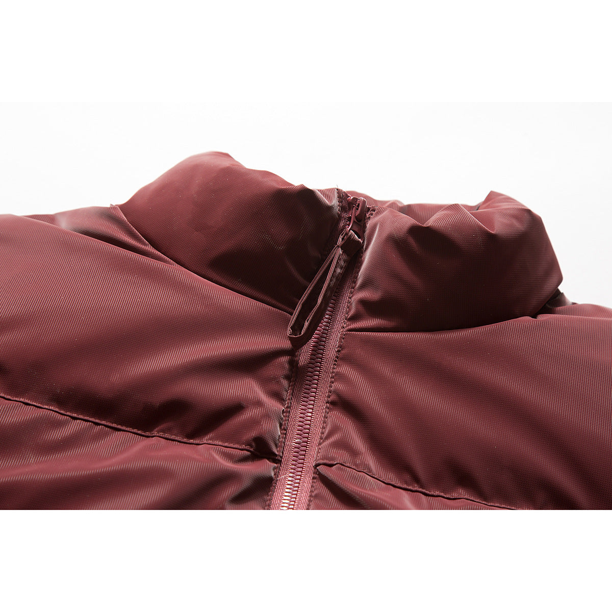Close-up of a burgundy puffer jacket showing its raised collar, front zipper and quilted panels.