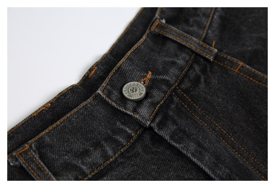 Close-up of the black jeans' waistband, belt loop, and metal button with a small embossed mark.