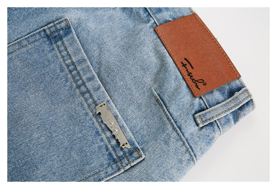 Close-up of light blue jeans showing a brown leather waistband patch, belt loop, pocket, and metal plate.