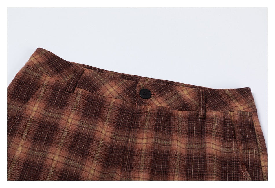 Close-up of the button, belt loops, and checked waistband of brown plaid trousers.