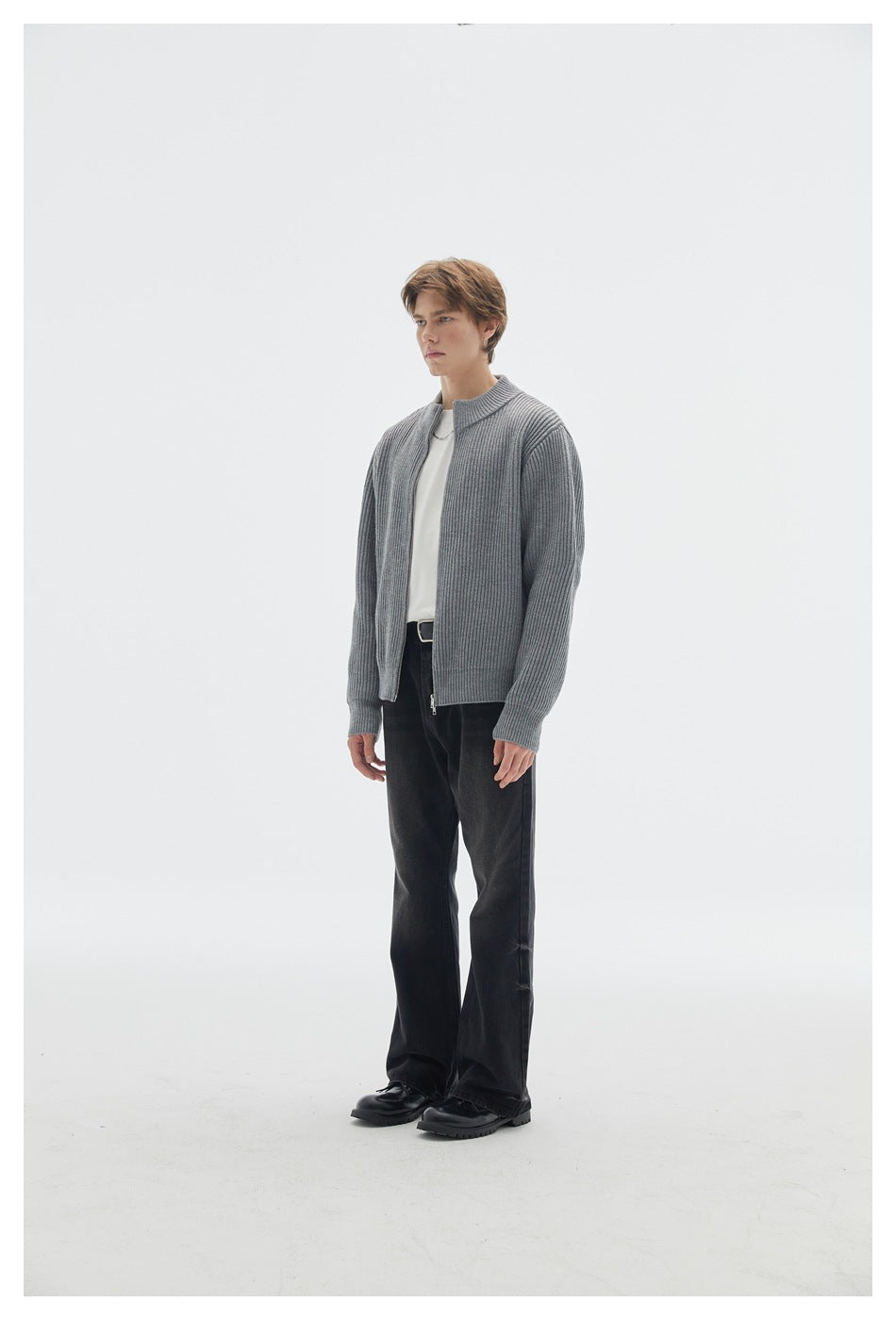 Three-quarter view of a model in a gray ribbed zip cardigan, white shirt, and black trousers.