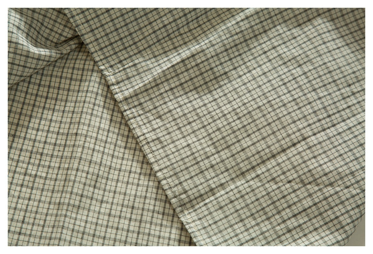 Close-up of cream plaid shirt fabric folded to show a stitched edge and hem.