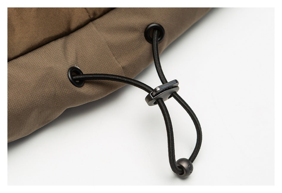 Close-up of a brown garment edge with black elastic drawcord, eyelets and an adjustable toggle.