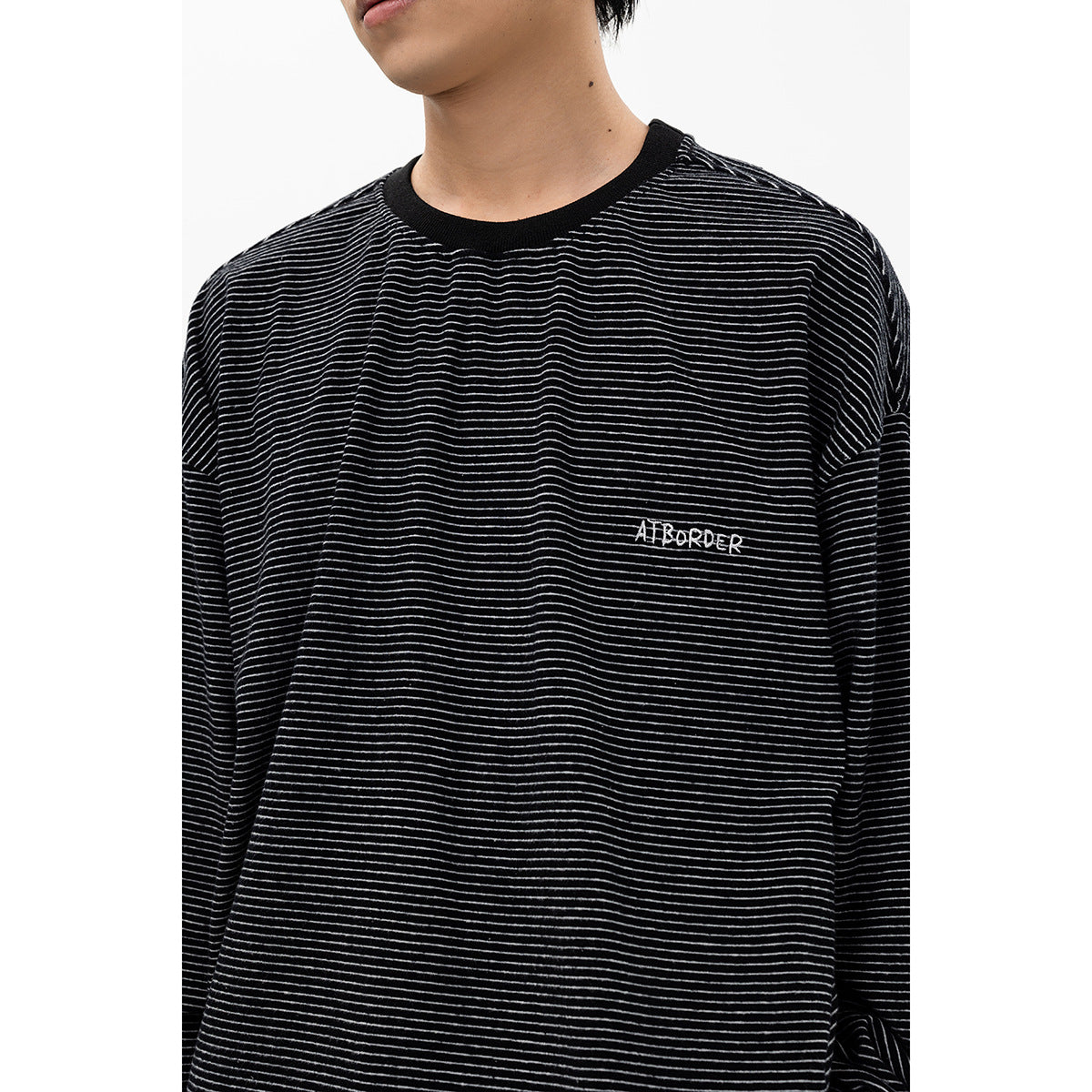 Close-up of a black shirt with thin gray stripes, a black crew neck, and small embroidered chest lettering.