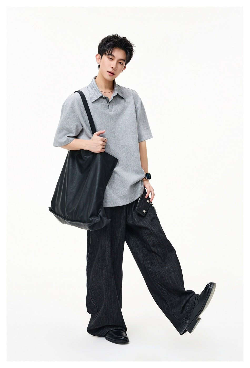Model wearing an oversized light gray short-sleeve polo shirt with a textured collar and dark wide-leg jeans.