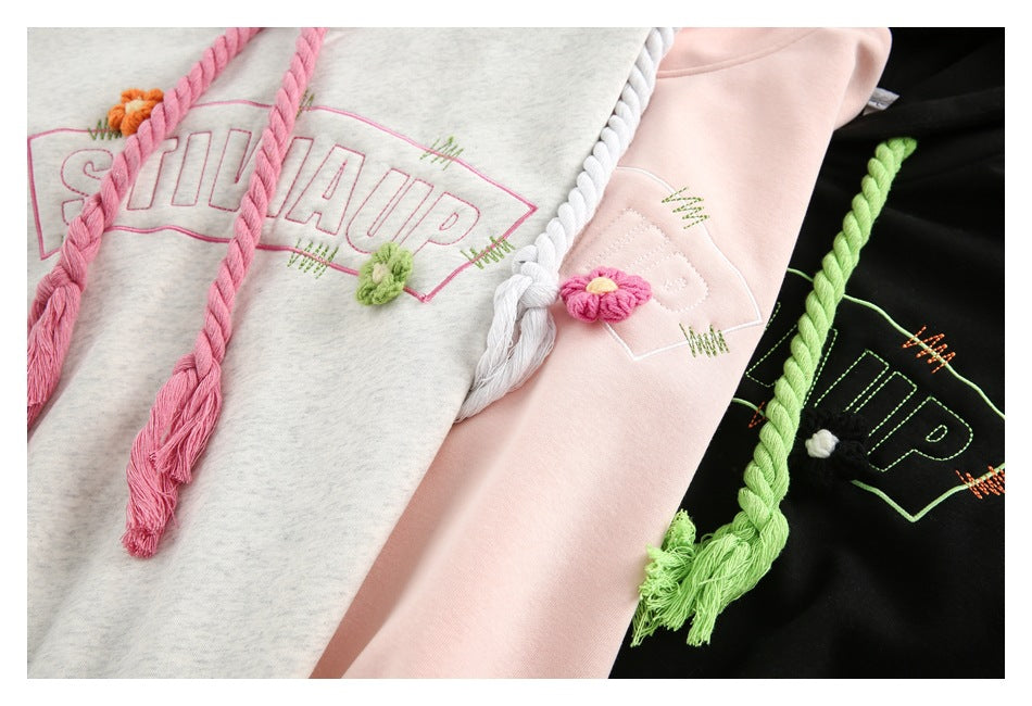 Close-up of three hoodies with colorful braided drawstrings and embroidered lettering and floral accents.