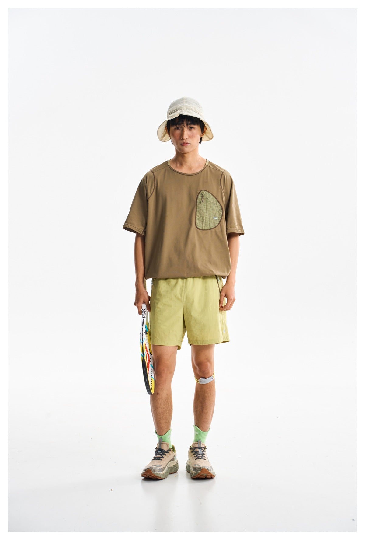 Front view of a model in a brown short-sleeve shirt with a chest pocket and light yellow-green shorts.