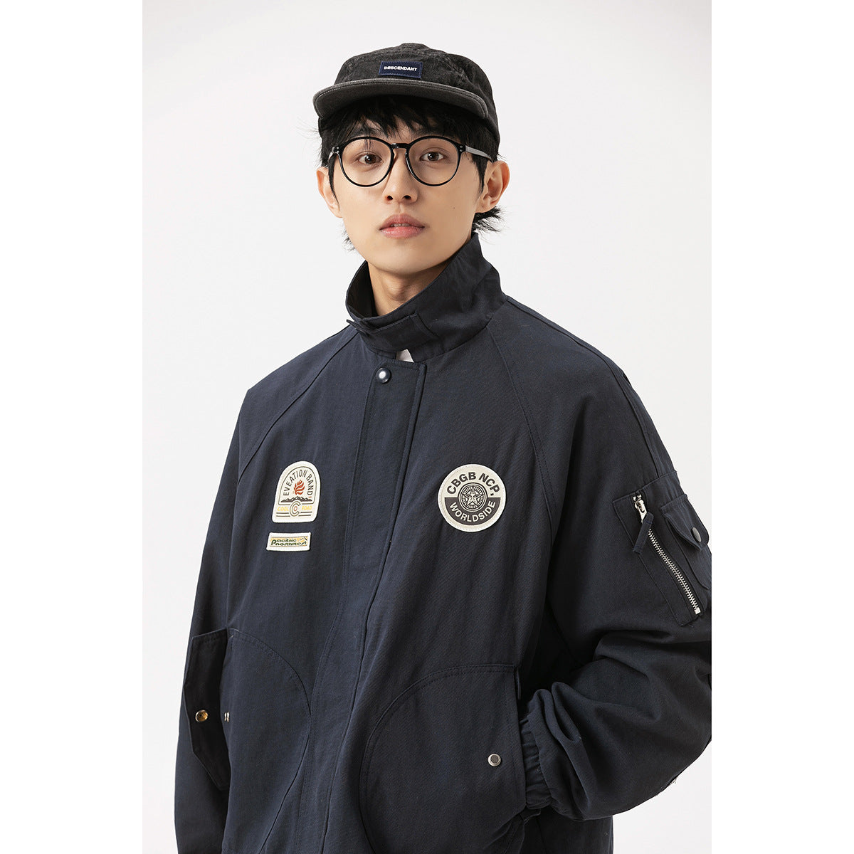 Close view of a model wearing a dark navy high-collar jacket with chest patches, large pockets and a zippered sleeve pocket.
