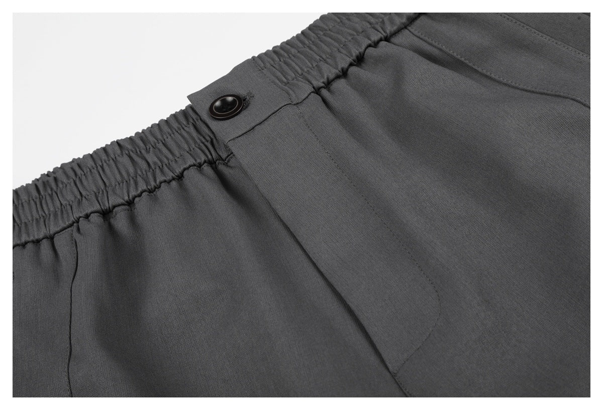 Close-up of charcoal shorts showing the elastic waistband, black button, and front closure stitching.